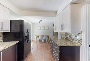 A kitchen with dark cabinets, a black refrigerator, a granite countertop, and a dining area with a table and chairs. - Bright and airy home with enclosed pool, hammock, and open-concept interior (Fort Myers)
