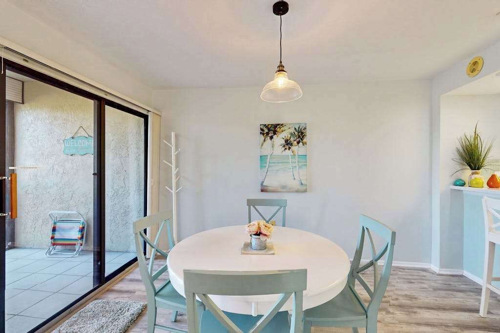 A dining area with a round table, chairs, a hanging light fixture, and a painting on the wall.