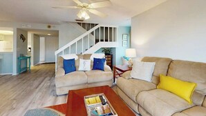 Ein Wohnzimmer mit einem beigefarbenen Sofa, einem Couchtisch und einer Treppe, die in eine weitere Ebene führt.