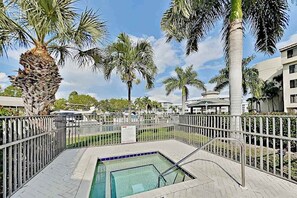 A swimming pool with a tiled deck, surrounded by palm trees and a metal fence. - Corner Unit Condo with Private Balcony, and Shared Pool - Walk to Beach (Fort Myers Beach)