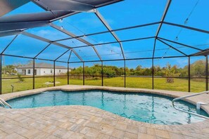 A swimming pool with a clear view of the surrounding landscape, a covered area with a metal roof, and a brick patio. - Renovated dog-friendly home near beach with private pool, screened lanai, grill (Englewood)