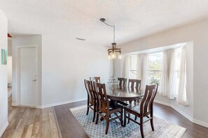 A dining room with a round table, six chairs, a chandelier, and a view through large windows. - Renovated dog-friendly home near beach with private pool, screened lanai, grill (Englewood)