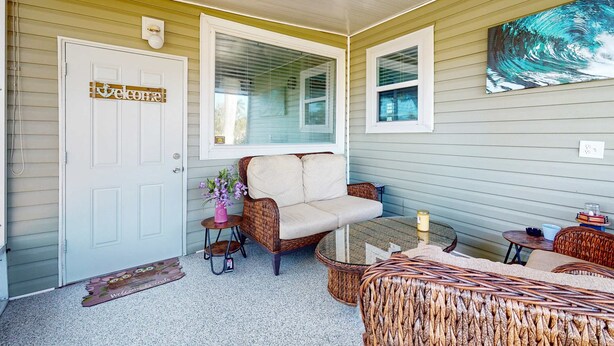 Eine überdachte Veranda mit einem Rattan-Sofa, einem kleinen Tisch und einem Rattan-Sessel.