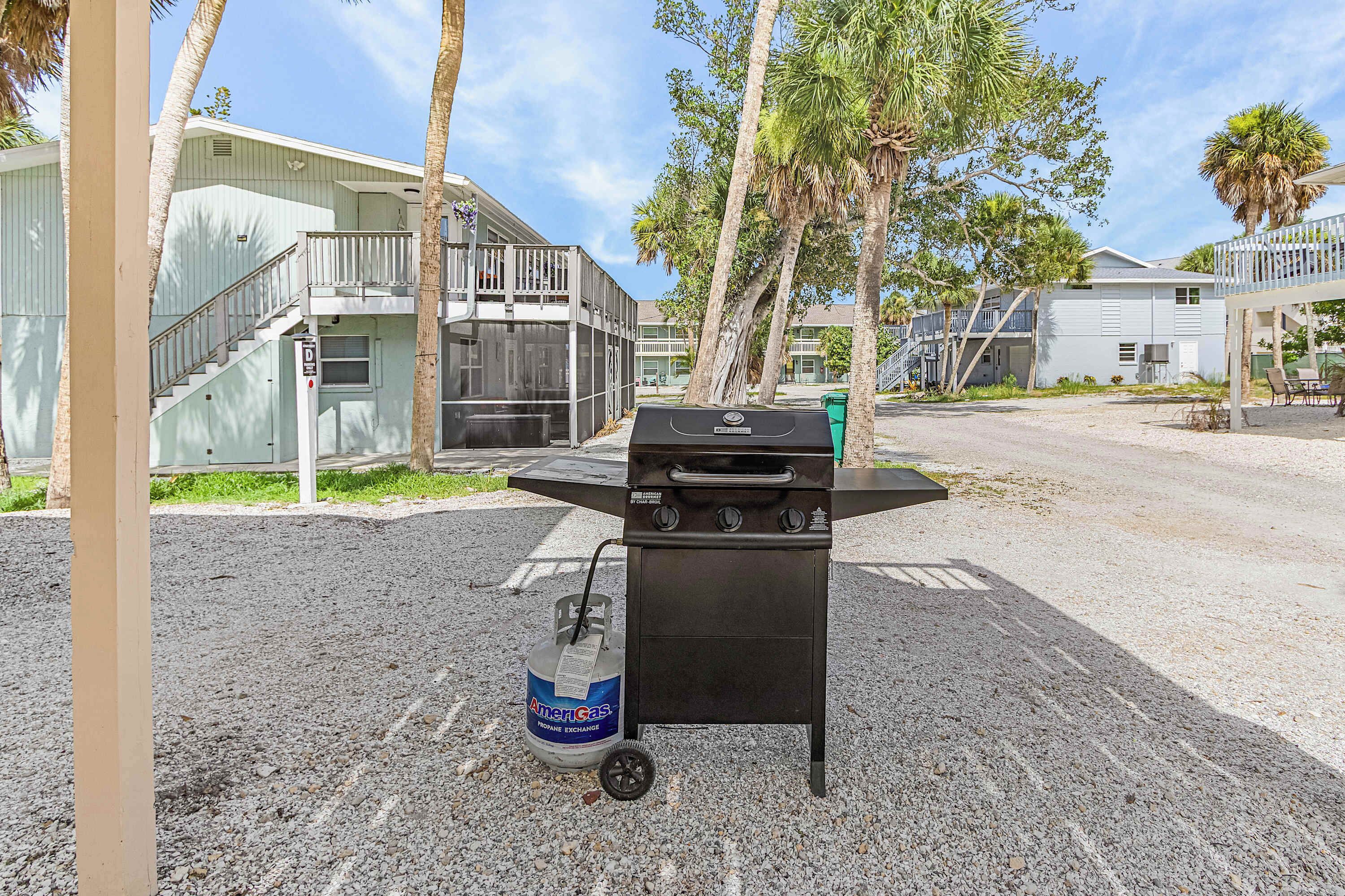 Un barbecue portatif avec une bouteille de propane, situé dans un parking avec des bâtiments en arrière-plan.