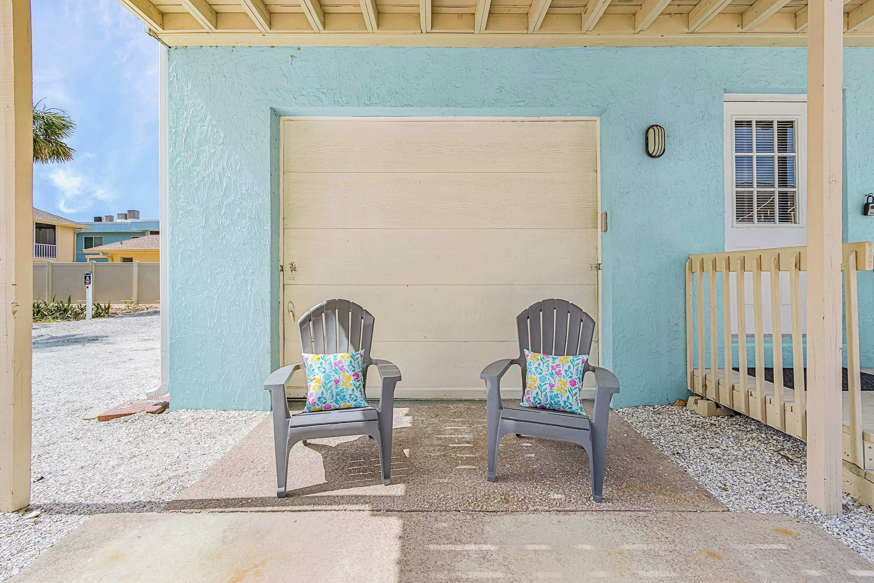 A covered porch with two Adirondack chairs and a garage door.