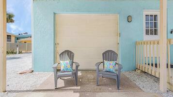 A covered porch with two Adirondack chairs and a garage door.