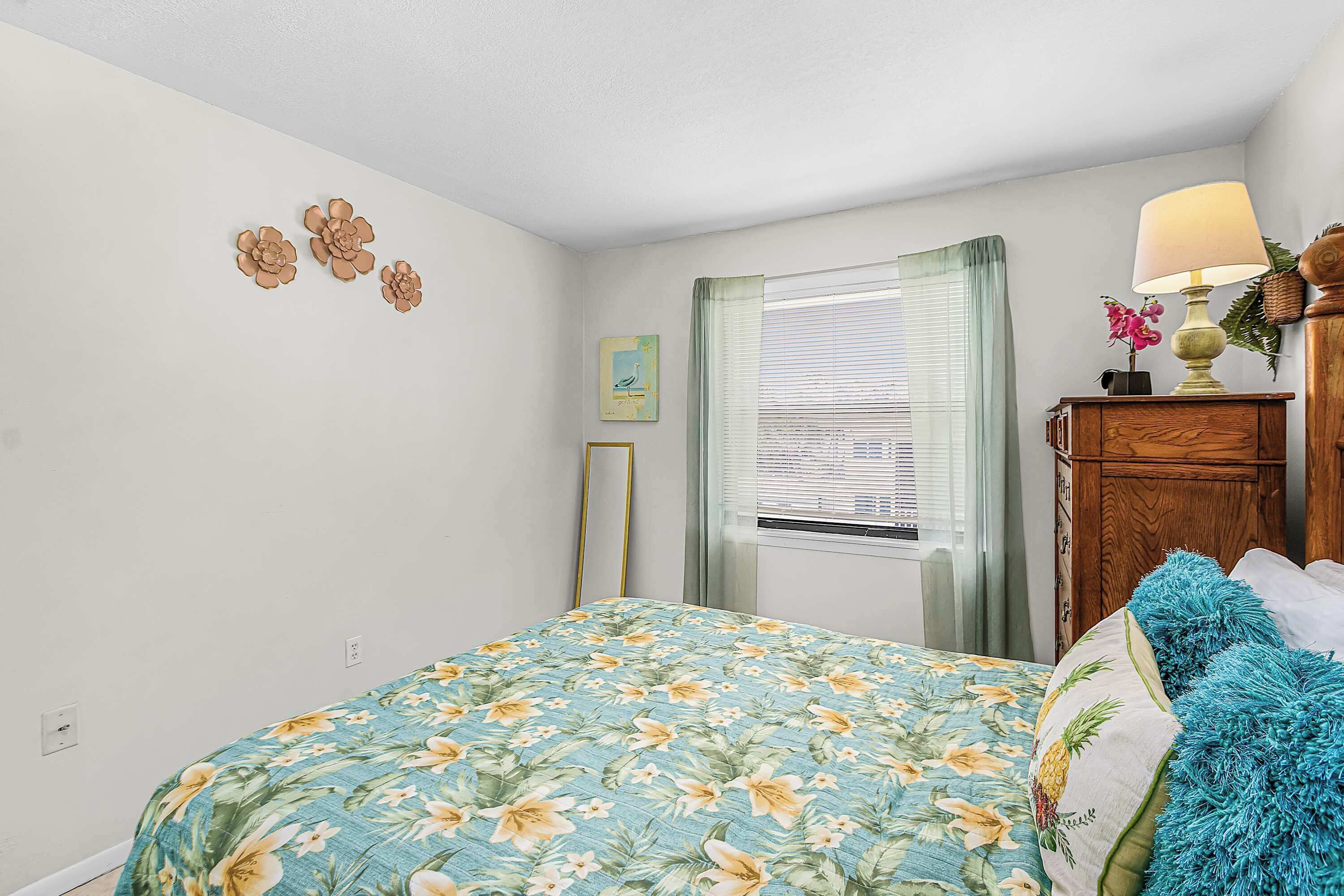 A bedroom with a bed, a dresser, a window with blinds, a lamp, and wall decorations.