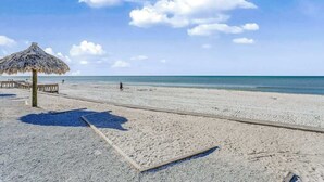 Een strand met een rieten parasol, een houten looppad en een heldere lucht.
