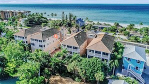 Een woongebied aan de kust met meerdere twee-onder-een-kapwoningen, een strand en helder uitzicht op de oceaan.
