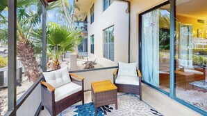 A balcony with wicker furniture, a glass door, and a view of a building and palm trees. - First-floor condo with shared pool, washer & dryer, beach access (Marco Island)