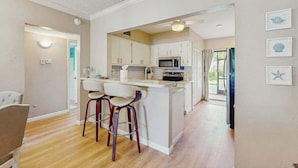 A modern kitchen with white cabinets, a central island with stools, and a microwave. - First-floor condo with shared pool, washer & dryer, beach access (Marco Island)