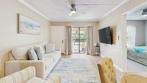 A spacious living room with a sofa, armchair, and a flat-screen TV mounted on the wall. - First-floor condo with shared pool, washer & dryer, beach access (Marco Island)