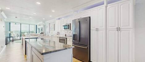 A modern kitchen with white cabinetry, stainless steel appliances, and a large island.