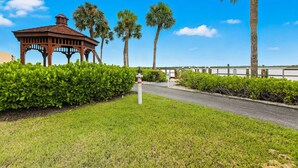 A gazebo with a tiled roof, surrounded by well-maintained hedges and palm trees. - Amazing oceanfront condo with pool, hot tub, dock, & views - snowbird-friendly (Marco Island)