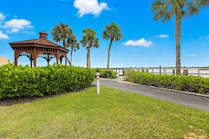 A gazebo with a tiled roof, surrounded by well-maintained hedges and palm trees.