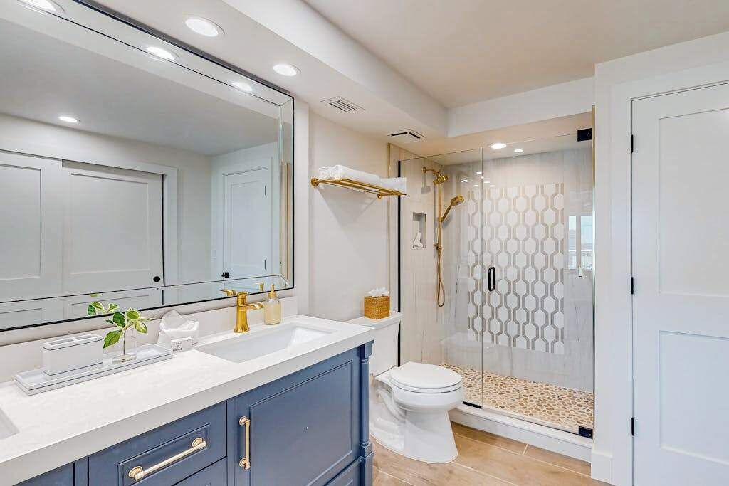 Un bagno moderno con un ampio specchio, due lavandini, un water e un'area doccia con pareti in vetro.