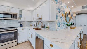 Een moderne keuken met witte kasten, een marmeren aanrechtblad en een decoratieve wand met blauwe bloemenbehang.