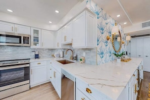 A modern kitchen with white cabinetry, a marble countertop, and a decorative wall with blue floral wallpaper. - Gulf-front getaway with on-site pool, tennis, putting green, dock, & gym (Marco Island)