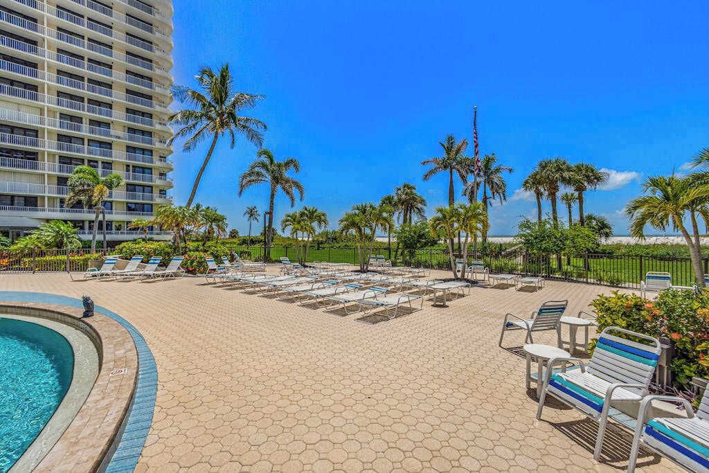 A hotel pool area with hexagonal tiles, lounge chairs, and palm trees.