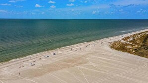 Luchtbeeld van een strand met heldere lucht, kalme zee en een zandstrand met begroeiing.