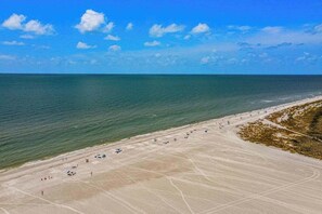 An aerial view of a beach with a clear sky, calm sea, and a sandy shore with some vegetation. - Gulf-front getaway with on-site pool, tennis, putting green, dock, & gym (Marco Island)