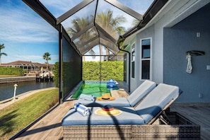 A glass-enclosed balcony with a pool, lounge chairs, and a view of a marina. - Waterfront house with private pool, dock, bikes, firepit, kayak & lanai (Marco Island)