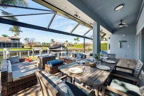 Un patio al aire libre con asientos, una mesa lista para comer y vistas al agua y casas circundantes.