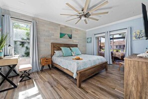 Un dormitorio con una cama de madera, un escritorio, una silla, un ventilador de techo y vistas al exterior.