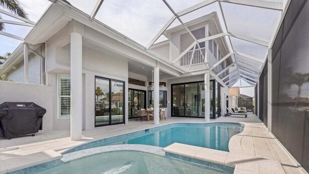 A swimming pool with a glass-enclosed patio area, a barbecue grill, and a covered outdoor seating area. - Waterfront home with private heated pool, spa, BBQ, views & bikes (Marco Island)