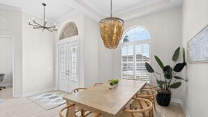 A dining area with a long table, chairs, a chandelier, and a potted plant. - Waterfront home with private heated pool, spa, BBQ, views & bikes (Marco Island)