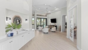 A spacious living area with a white reception desk, seating, a ceiling fan, and a television. - Waterfront home with private heated pool, spa, BBQ, views & bikes (Marco Island)