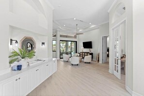 A spacious living area with a white reception desk, seating, a ceiling fan, and a television. - Waterfront home with private heated pool, spa, BBQ, views & bikes (Marco Island)