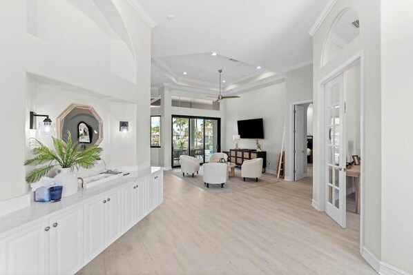 A spacious living area with a white reception desk, seating, a ceiling fan, and a television. - Waterfront home with private heated pool, spa, BBQ, views & bikes (Marco Island)
