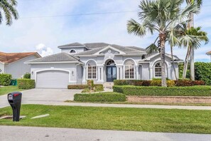A single-story house with a garage, a front porch, and a well-maintained lawn. - Waterfront home with private heated pool, spa, BBQ, views & bikes (Marco Island)