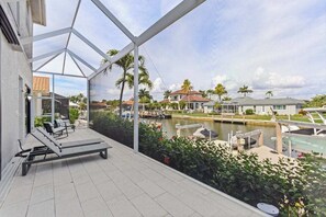 A covered outdoor area with a lounge chair, a view of a canal with boats, and houses in the background. - Waterfront home with private heated pool, spa, BBQ, views & bikes (Marco Island)