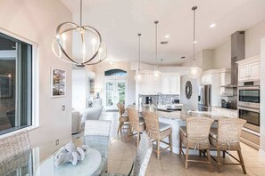 A modern kitchen with a central island, pendant lighting, and a dining area with wicker chairs. - Luxurious, waterfront home with private pool/spa (Marco Island)