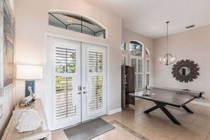 A spacious room with a ping pong table, a door with glass panels, and a decorative mirror. - Luxurious, waterfront home with private pool/spa (Marco Island)