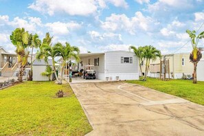 A mobile home with a driveway, palm trees, and a clear sky.