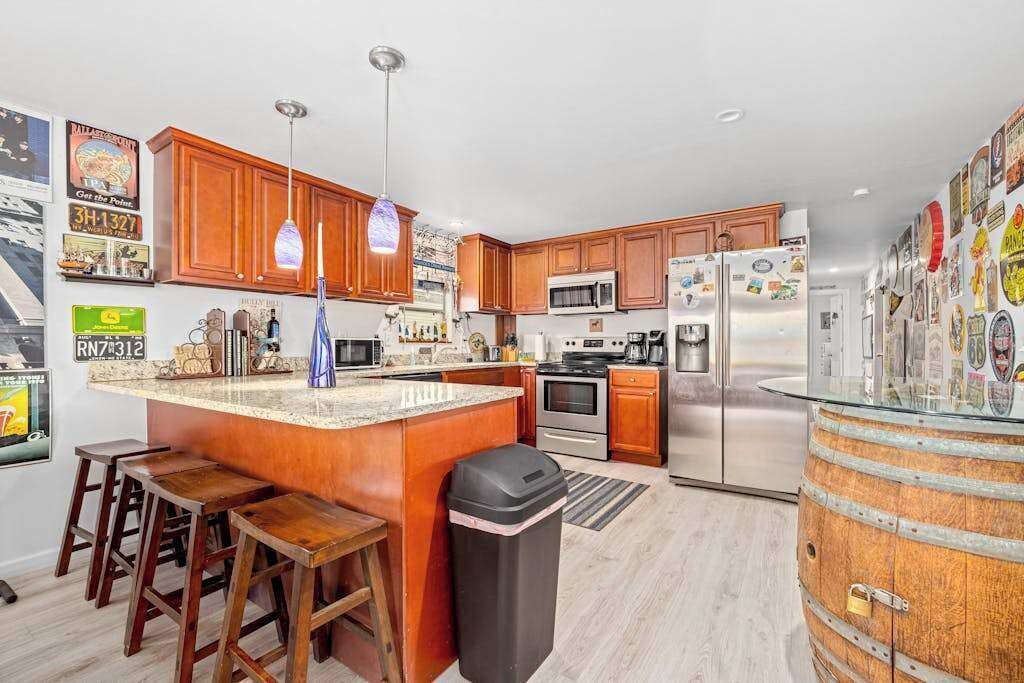 A kitchen with wooden cabinets, a central island with stools, stainless steel appliances, and a barrel.