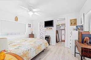 A bedroom with a bed, a ceiling fan, a TV, a dresser, and a desk.
