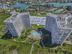 A high-rise hotel with a curved facade, a central courtyard with a pool, and surrounding greenery. - Coastal Condo W/ Beach Access, Shared Pool, Private Balcony & Fast WiFi (Marco Island)