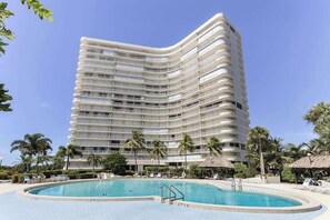 A multi-story hotel with a pool area, palm trees, and a clear sky. - Coastal Condo W/ Beach Access, Shared Pool, Private Balcony & Fast WiFi (Marco Island)
