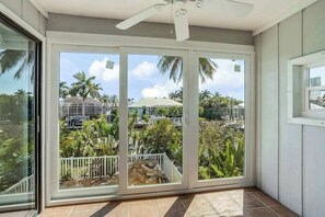 A room with a sliding glass door leading to a balcony with a view of palm trees and a distant building. - Canal-front home with private lagoon pool, dock, AC, & W/D - dog-friendly (Marco Island)