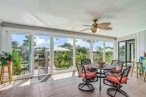 A sunlit patio with a table and chairs, large windows, and a ceiling fan. - Canal-front home with private lagoon pool, dock, AC, & W/D - dog-friendly (Marco Island)
