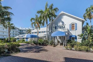 A hotel with a white exterior, blue shutters, and a covered outdoor area with umbrellas. - Renovated condo with screened balcony, AC, & shared pool/spa/sundeck (Marco Island)