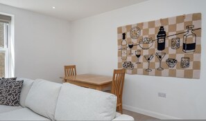 A modern living room with a checkered wall art, a wooden dining table, and a white sofa. - New 1 Bed Flat Near Central London With Terrace (London)