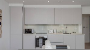 A modern kitchen with white cabinets, a built-in oven, a microwave, a coffee maker, and a sink. - New 1 Bed Flat Near Central London With Terrace (London)
