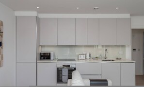 A modern kitchen with white cabinets, a built-in oven, a microwave, a coffee maker, and a sink. - New 1 Bed Flat Near Central London With Terrace (London)