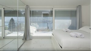 A modern hotel room with a large bed, a balcony with a view, and a glass partition. - Open View Apartment by Wonderful Italy (Oliveto Lario)