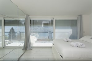 Een moderne hotelkamer met een groot bed, een balkon met uitzicht en een glazen scheiding.